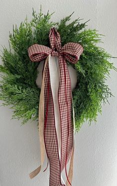 a christmas wreath hanging from the side of a white wall with red and tan ribbon