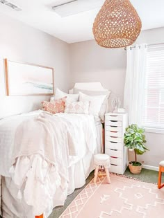 a bedroom with white bedding and pink accents on the walls, an area rug, and a hanging light fixture