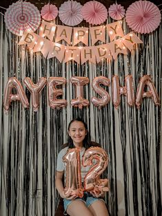 a woman sitting in front of a wall with balloons and streamers on it that say happy birthday ayeesha