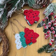 three crocheted ornaments on a wooden table next to pine cones and evergreen branches