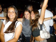 three young women standing next to each other in front of a group of people at a party