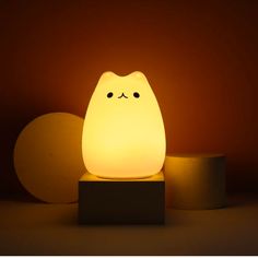 a white cat lamp sitting on top of a wooden block next to an orange wall