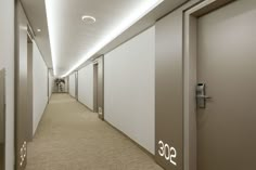 an empty hallway with white walls and beige carpeted flooring is seen in this image