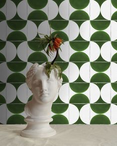 a white vase with a flower in it on a table next to a green and white wall