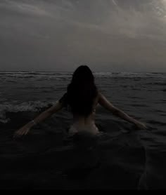 a woman is in the water with her arms spread out and looking at the sky