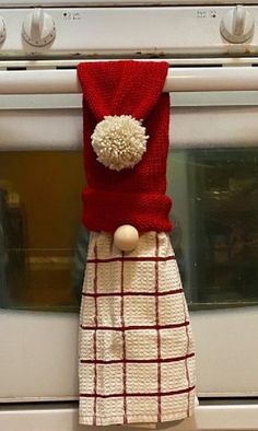 a red and white towel hanging from the side of a stove top oven with a pom - pom on it's head