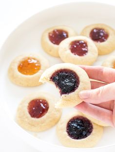 a hand holding a cookie with jam on it in front of other cookies and jelly