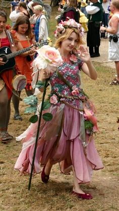 a woman in a dress holding a flower and walking through a field with other people