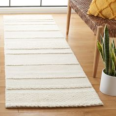 a large white rug on the floor next to a chair and potted plant in front of a window