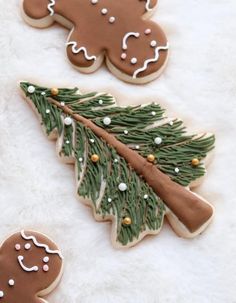 three decorated cookies on top of a white furnishing next to a christmas tree