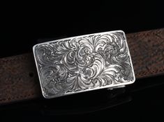 One of our most popular buckles, this understated piece by Comstock Heritage is perfect for those just starting their buckle collections, or for more formal occasions. It’s made from heavy-gauge, hand-engraved Sterling silver, and its rectangular face is adorned with beautiful, delicate scrollwork. This buckle can be paired easily blue jeans or be worn with dressier slacks. Smaller size measures 1 ⅝” x 2 ⅝” and fits all 1 ¼" belt traps Larger version measures 1 ⅞” x 2 ¾" and fits all 1 ½" belt s Luxury Engraved Silver Belt Buckles, Classic Engraved Belts For Formal Occasions, Classic Formal Belts With Engraved Details, Classic Formal Belt With Engraved Details, Classic Formal Engraved Belt, Luxury Formal Jewelry With Silver Buckle, Rectangular Engraved Silver Belt Buckles, Silver Engraved Rectangular Belt Buckles, Rectangular Silver Engraved Belt Buckles