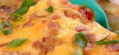 a close up of a cheesy casserole dish with green onions and bacon