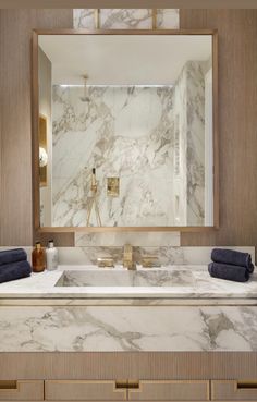 a bathroom with marble counter tops and gold trim on the mirror, along with blue towels