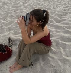 a woman sitting in the sand taking a photo with her cell phone