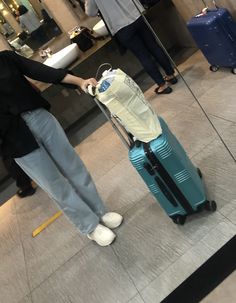 a woman standing next to a blue suitcase in an airport lobby with her hand on the handle