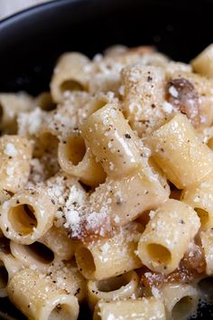 a black bowl filled with pasta covered in powdered sugar