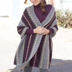 a woman is walking down the street wearing a purple and gray ponchy shawl