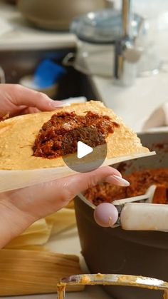 a person holding a tortilla in their hand with chili on top and meat inside