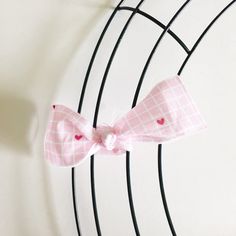 a pink bow with hearts on it sitting on top of a wire rack in front of a white wall