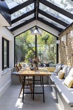 a table and benches in a room under a roof with glass walls that overlook the garden