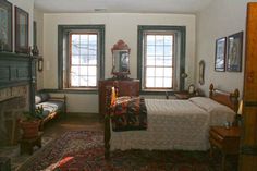 a bed room with a neatly made bed next to two windows and a rug on the floor