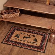 welcome to our cabin door mat on the floor next to a potted plant and pine cones