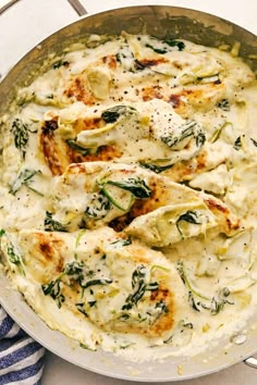 a skillet filled with cheese and spinach covered in cream sauce on top of a blue and white checkered table cloth