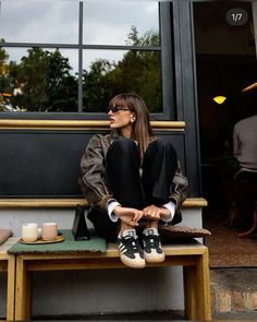 a woman sitting on top of a wooden bench next to a table with coffee cups