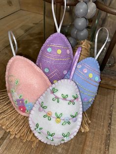 three decorative easter eggs hanging from strings on a wooden table next to some beads and string