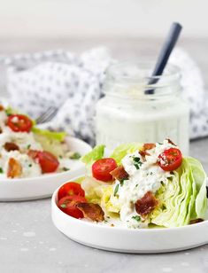 two white bowls filled with lettuce and tomatoes next to a jar of dressing