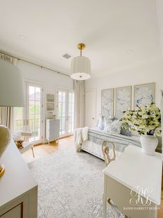 a bedroom with white furniture and paintings on the wall, along with a large rug