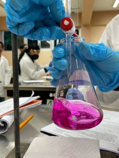 a person in blue gloves holding a flask filled with pink liquid on top of a table