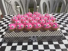 cupcakes with pink frosting and googly eyes are on a checkered tablecloth