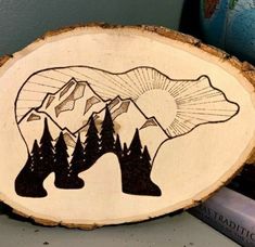 a bear is standing in front of some trees and mountains on a wood slice that has been carved into the shape of a mountain