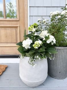 two large white vases with green and white flowers on the front porch next to a door