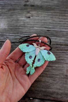 a hand holding a small green butterfly on a string