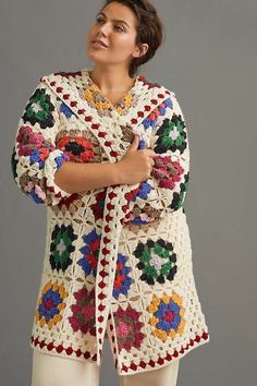 a woman standing with her arms crossed and wearing a crocheted sweater over her shoulders