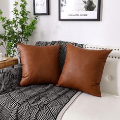 two brown pillows sitting on top of a white couch next to a potted plant