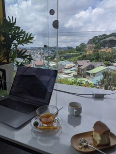 a laptop computer sitting on top of a table next to a plate of food and cup