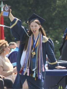 a woman wearing a graduation gown and holding her arms in the air while standing next to other people