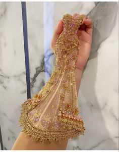 a person holding up a dress made out of gold sequins in front of a mirror