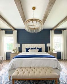 a bedroom with blue walls, white bedding and a chandelier hanging from the ceiling