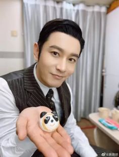 a man in a vest and tie holding a small toy panda bear on his finger