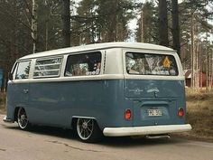 an old vw bus is parked on the side of the road in front of some trees