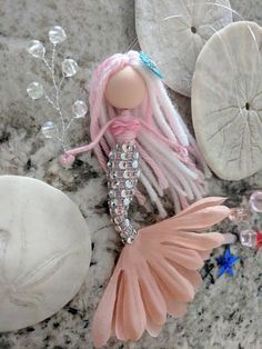 an assortment of sea shells and accessories on a marble counter top, including a doll with pink hair