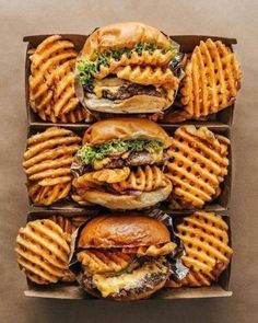 three boxes filled with hamburgers and waffle fries on top of each other in front of them