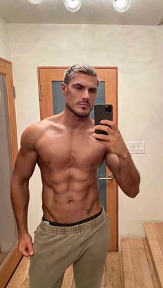 a shirtless man taking a selfie in front of a mirror with his cell phone