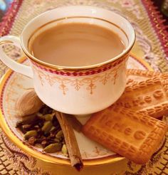 there is a cup of tea and some cookies on the plate with cinnamon sticks next to it