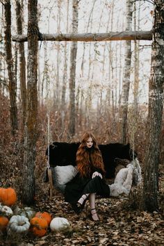 a woman sitting on a swing in the woods surrounded by pumpkins and other fall foliage