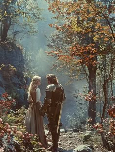 a man and woman dressed in medieval clothing standing next to each other on a forest path